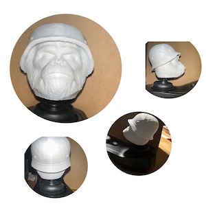 May include: A white sculpture of a chimpanzee head wearing a helmet. The sculpture is mounted on a black base. Additional views of the sculpture are shown in smaller circular frames. The background is a light brown color.