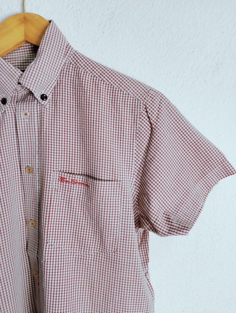 K&ouml;nnte beinhalten: Ein kurz&auml;rmeliges Hemd mit Knopfleiste und einem rot-wei&szlig;en Vichy-Karo-Muster. Das Hemd verf&uuml;gt &uuml;ber einen Button-Down-Kragen, eine Brusttasche mit dem roten Sticktext Ben Sherman und helle Kn&ouml;pfe entlang der vorderen Knopfleiste.