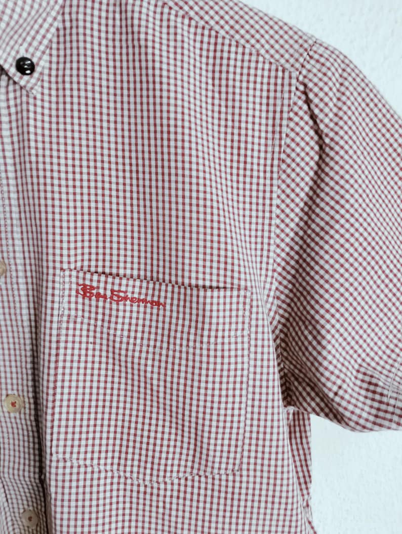 K&ouml;nnte beinhalten: Ein kurz&auml;rmeliges Hemd mit Knopfleiste und einem rot-wei&szlig;en Gingham-Karomuster. Das Hemd verf&uuml;gt &uuml;ber eine Brusttasche mit dem in rotem Garn gestickten Schriftzug Ben Sherman dar&uuml;ber sowie helle Kn&ouml;pfe entlang der vorderen Knopfleiste.