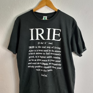 May include: Black t-shirt with the word "IRIE" in large white letters. Below the word is a definition, also in white, explaining the term's meaning and usage. The shirt is hanging on a wooden hanger.