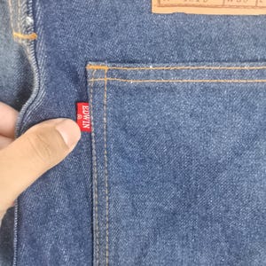 Puede incluir: Primer plano de unos vaqueros de mezclilla azules con un bolsillo trasero y una etiqueta roja de Edwin. La etiqueta Edwin tambi&eacute;n es visible en la parte trasera de los vaqueros. Los vaqueros tienen una etiqueta de cuero marr&oacute;n con el texto "EDWIN THE EDWIN COMPANY 1015 W30".