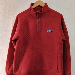 Puede incluir: Un jersey rojo acolchado con cuello alto y cierre de botones. El jersey tiene un pequeño logotipo de parche en el pecho izquierdo que dice "L.L.Bean".