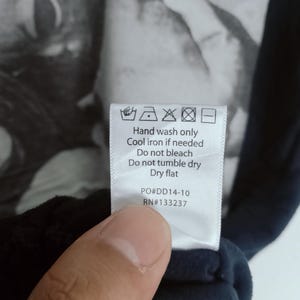 May include: A close-up of a care label with washing instructions and the text "Hand wash only, Cool iron if needed, Do not bleach, Do not tumble dry, Dry flat." The label also includes the codes PO#DD14-10 and RN#133237.