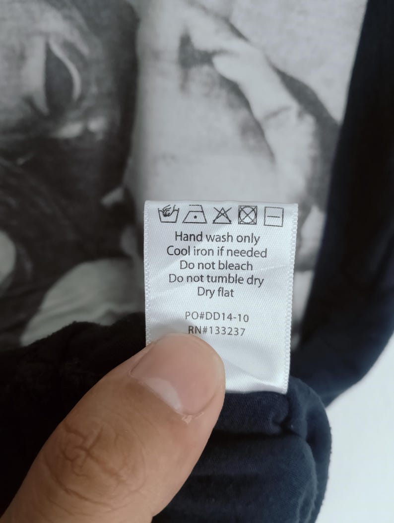 May include: A close-up of a care label with washing instructions and the text "Hand wash only, Cool iron if needed, Do not bleach, Do not tumble dry, Dry flat." The label also includes the codes PO#DD14-10 and RN#133237.