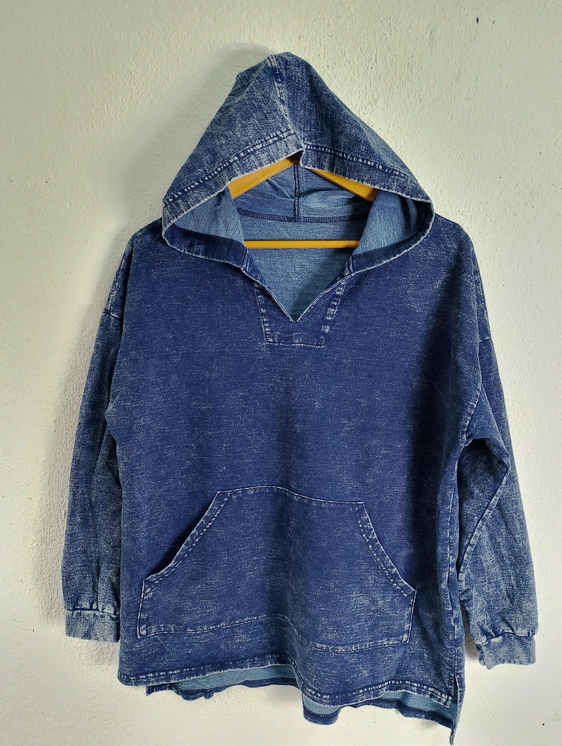 Pode incluir: Um moletom azul jeans com bolso frontal e capuz. O moletom tem decote em V e mangas compridas. O jeans tem uma apar&ecirc;ncia desbotada e texturizada.
