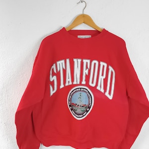 Könnte beinhalten: Ein rotes Sweatshirt der Stanford University mit weißen Buchstaben und einem kreisförmigen Emblem. Das Wort "STANFORD" ist über der Brust gewölbt. Das Emblem zeigt einen Baum und die Worte "LELAND STANFORD JUNIOR UNIVERSITY" und "ORGANIZED 1891".