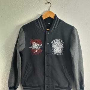 Puede incluir: Chaqueta de béisbol negra y gris con un gráfico rojo y blanco en la manga izquierda que dice "Man Kata Round One Crew" y un gráfico blanco en la manga derecha que dice "Maximum 30x more".