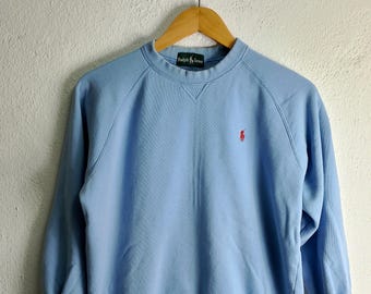 May include: A light blue sweatshirt with a small red polo player logo on the left chest. The text "Ralph Lauren" is visible on the neck tag.