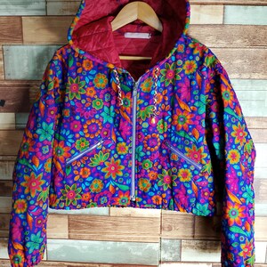 Könnte beinhalten: Eine blaue gesteppte Jacke mit Blumenmuster und einer roten Kapuze. Die Jacke hat einen Reißverschluss und zwei Taschen.
