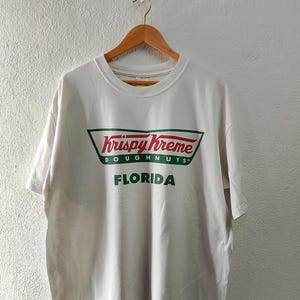 May include: White t-shirt with a green and red Krispy Kreme Doughnuts logo and the text "Florida".