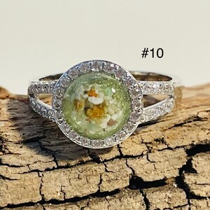 Könnte beinhalten: Silberring mit einem klaren runden Besatz, der mit grünen und weißen Steinen besetzt ist. Der Ring hat eine doppelte Band und ist mit kleinen klaren Steinen um den Besatz herum besetzt. #10