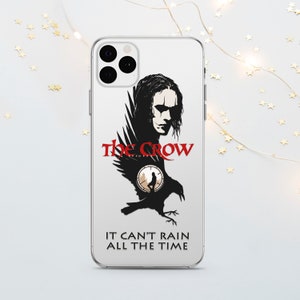 Puede incluir: Una funda transparente para teléfono con una ilustración en blanco y negro del personaje de The Crow de la película. El texto "The Crow" está en rojo y la cita "It can't rain all the time" está debajo de la ilustración.