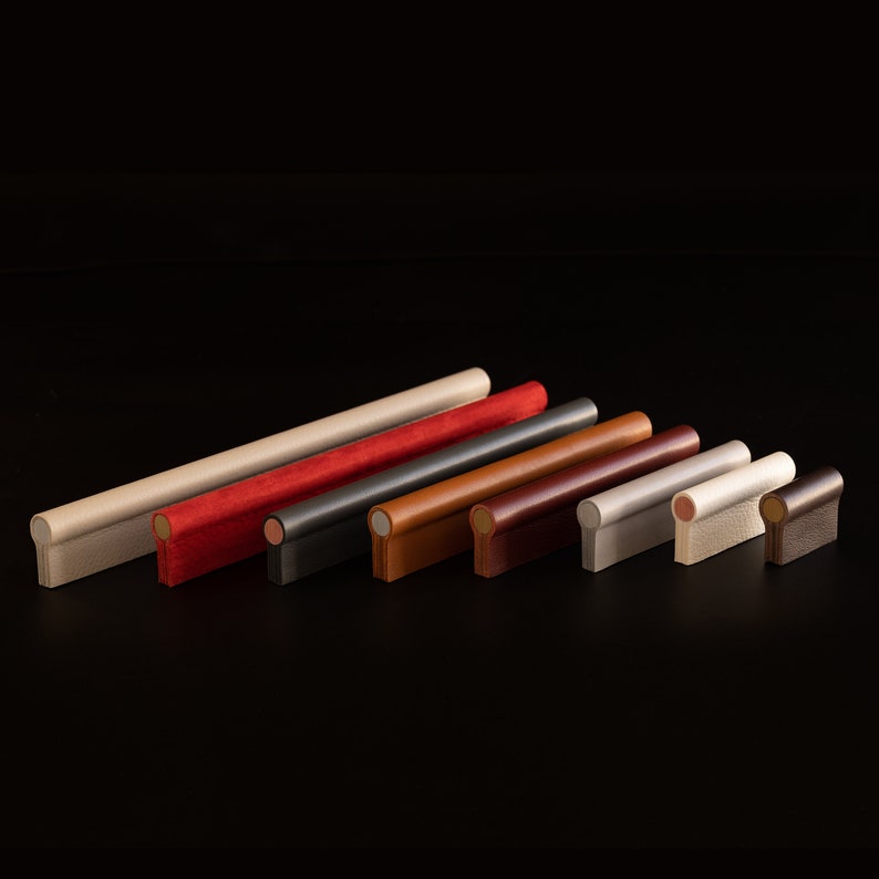 May include: A set of eight leather drawer pulls in various colors, including beige, red, black, brown, and gray. The pulls are all cylindrical with rounded ends.