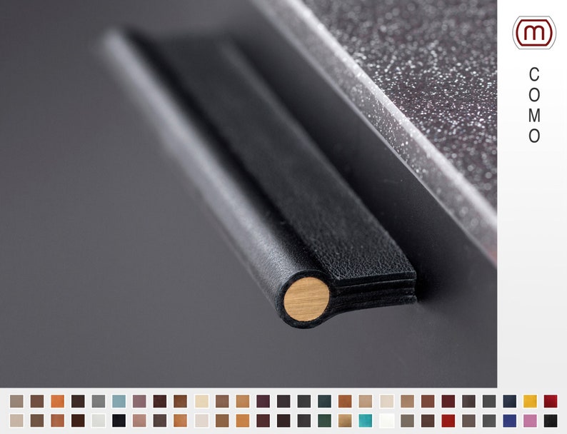 May include: Black leather cabinet pull with a gold metal accent. The pull is mounted on a dark gray surface.