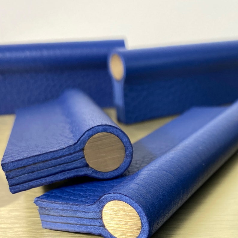 May include: Close-up of four blue leather drawer pulls with brass accents. The pulls are stacked on top of each other, with the top pull partially obscured by the others.