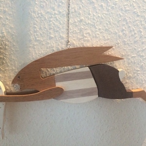 Könnte beinhalten: Eine hölzerne Hasenfigur, bemalt in Braun, Weiß und Schwarz, die eine weiße Karotte mit grünen Blättern hält. Die Karotte trägt die Aufschrift "Rabbit".