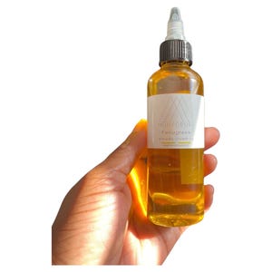 May include: A clear glass bottle filled with a golden liquid, held in a hand. The bottle has a white label with the text "MONKORIVER Fenugreek Extreme Growth Oil". The bottle has a black and white applicator top. The product is for hair care.