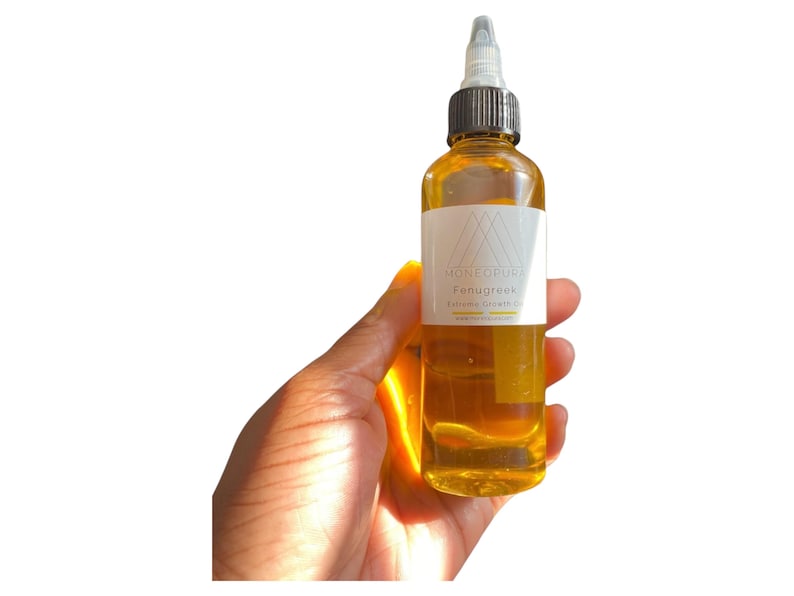 May include: A clear glass bottle filled with a golden liquid, held in a hand. The bottle has a white label with the text "MONKORIVER Fenugreek Extreme Growth Oil". The bottle has a black and white applicator top. The product is for hair care.