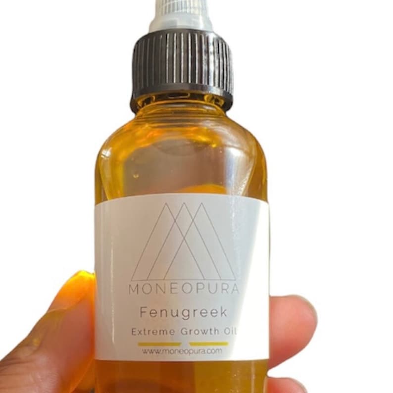 May include: A clear glass bottle filled with amber-colored oil. The bottle has a black cap and a white label with the text "MONEOPURA Fenugreek Extreme Growth Oil" and a website address. The bottle is held by a hand.
