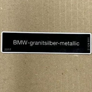 May include: A black label with white text that reads "BMW-granitsilber-metallic" and the numbers "2124 911" on the right side. The label has the number "237/7" on the left side.