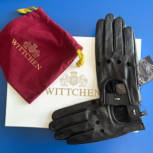 Peut inclure: Une paire de gants de conduite en cuir noir avec une boîte blanche et un sac en velours rouge. La boîte et le sac portent le logo Wittchen.