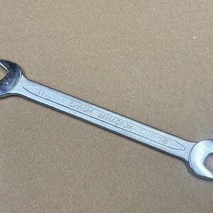Puede incluir: Una llave de cromo vanadio plateada, con extremos abiertos de tamaños 11 y 10. La herramienta está diseñada para apretar o aflojar tuercas y pernos. El texto "CHROM VANADIUM" está impreso en la llave.