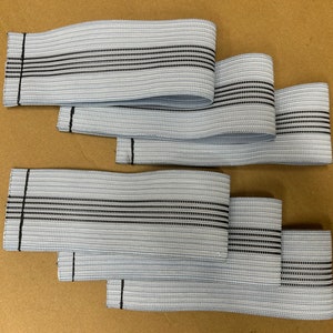 May include: Five pieces of light blue elastic with black stripes. The elastic is folded in half and stacked on top of each other.