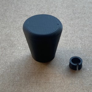 Może przedstawiać: Czarny plastikowy gałka z okrągłym wierzchołkiem i zwężającą się podstawą. W zestawie znajduje się również czarny plastikowy pierścień.