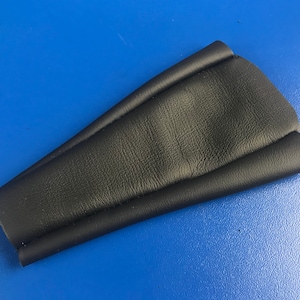 May include: A black leather item with a curved shape, possibly a component of a larger product. The leather has a textured surface and is set against a blue background. The item appears to be folded or stitched.