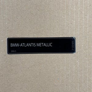 May include: A black rectangular label with white text that reads "BMW-ATLANTIS METALLIC" and the number "399/5" below the text. The label also has the number "2122615" printed vertically on the right side.