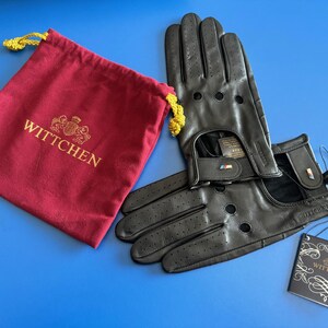 May include: Black leather driving gloves with perforations and a red and blue stripe detail. The gloves are paired with a red pouch with the word "WITTCHEN" embroidered in gold.
