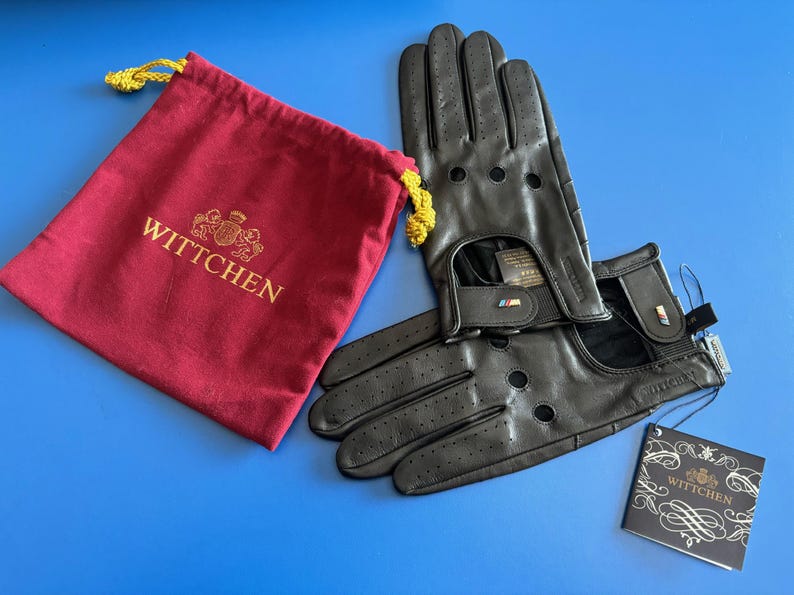 May include: Black leather driving gloves with perforations and a red and blue stripe detail. The gloves are paired with a red pouch with the word "WITTCHEN" embroidered in gold.
