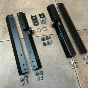 Puede incluir: Cuatro soportes de metal negro con múltiples agujeros y un pestillo de metal plateado. Los soportes están dispuestos en una fila sobre una superficie de azulejos. También hay varios tornillos y arandelas de metal plateado esparcidos alrededor de los soportes.