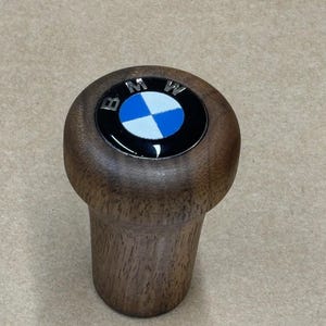 Puede incluir: Una palanca de cambios de madera con un logotipo BMW negro y azul en la parte superior.