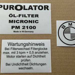 May include: Three white stickers with black text on a brown background. The top sticker reads "PUROLATOR ÖL-FILTER MICRONIC PM 2100 Made in W.Germany". The bottom sticker has German text. A BMW logo sticker is on the right.