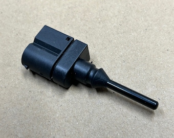 Puede incluir: Un sensor de temperatura automotriz negro con un conector y una sonda larga y delgada.