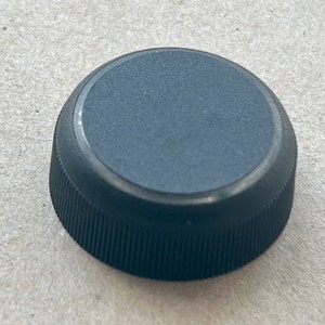 May include: Black plastic bottle cap with a ribbed edge.