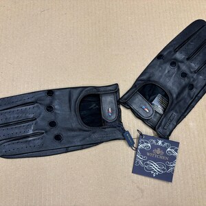 May include: A pair of black leather driving gloves with a perforated design and a small logo tag that reads "WITTCHEN".
