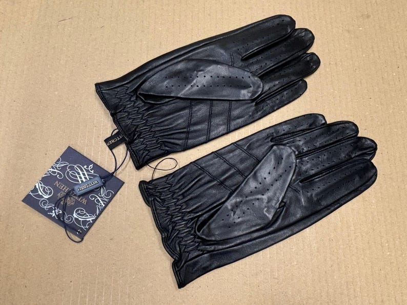 May include: A pair of black leather driving gloves with a textured surface and a small tag that says "The Collection".