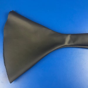 Op de afbeelding: Een kegelvormig object van zwart leer met een lange, smalle handgreep. Het object is gemaakt van een zacht, buigzaam materiaal en heeft een gladde, gelijkmatige textuur.