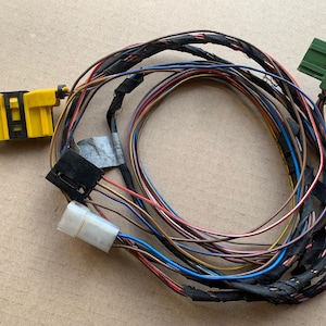 May include: A bundle of wires with black, brown, red, blue, and yellow insulation. The wires are bundled together with black tape. There are three connectors on the wires: one yellow, one white, and one green.