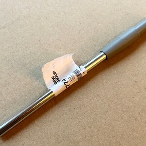 May include: A silver metal rod with a gray plastic handle. The rod has a label attached to it that reads "774 IMW GROUP".