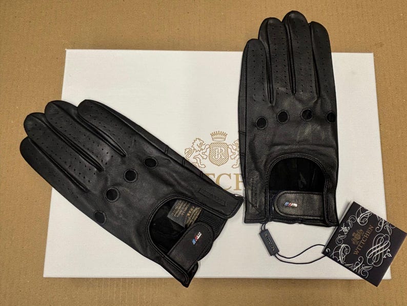 May include: Two pairs of black leather driving gloves with a perforated design. The gloves have a wrist strap and a small logo on the strap.