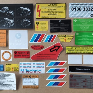 May include: A collection of stickers and labels for a car, featuring various warnings, instructions, and logos. The stickers are in German and English, and include phrases like "Achtung!" and "Super Bleifrei Tanken".