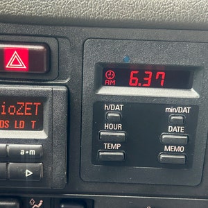 Puede incluir: Un salpicadero de coche negro con un reloj digital rojo que muestra las 18:37. El salpicadero también tiene un botón rojo de luces de emergencia, una pantalla de radio con el texto "RadioZET" y botones para RDS, LD y T, y una serie de botones etiquetados como "h/DAT", "HOUR", "TEMP", "min/DAT", "DATE" y "MEMO".