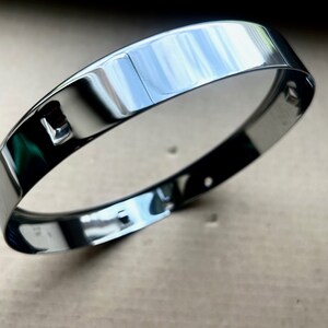 Könnte beinhalten: Ein glänzender silberner Metallring mit glatter, polierter Oberfläche. Der Ring hat ein kleines Loch oben.