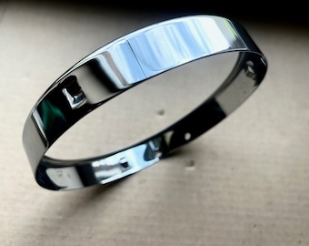 May include: A shiny silver metal ring with a smooth, polished finish. The ring has a small hole on the top.