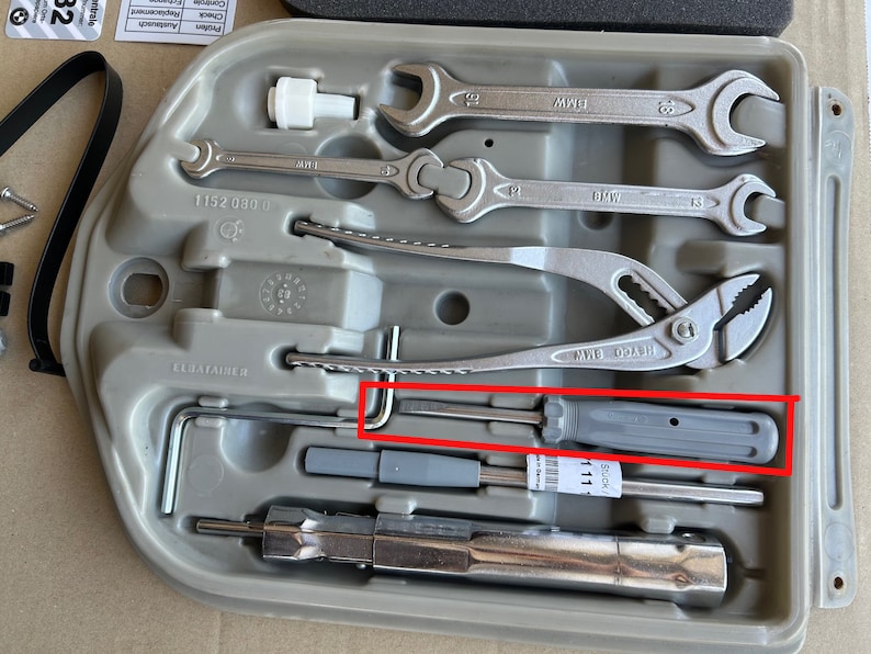 May include: A gray plastic tool kit with a variety of tools, including wrenches, pliers, and a screwdriver. The kit is labeled "BMW" and "ELDATALHER".