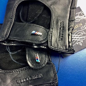 May include: A pair of black leather driving gloves with a blue, white, and red accent on each glove. The gloves have the text "WITTCHEN" embossed on the back of each glove.