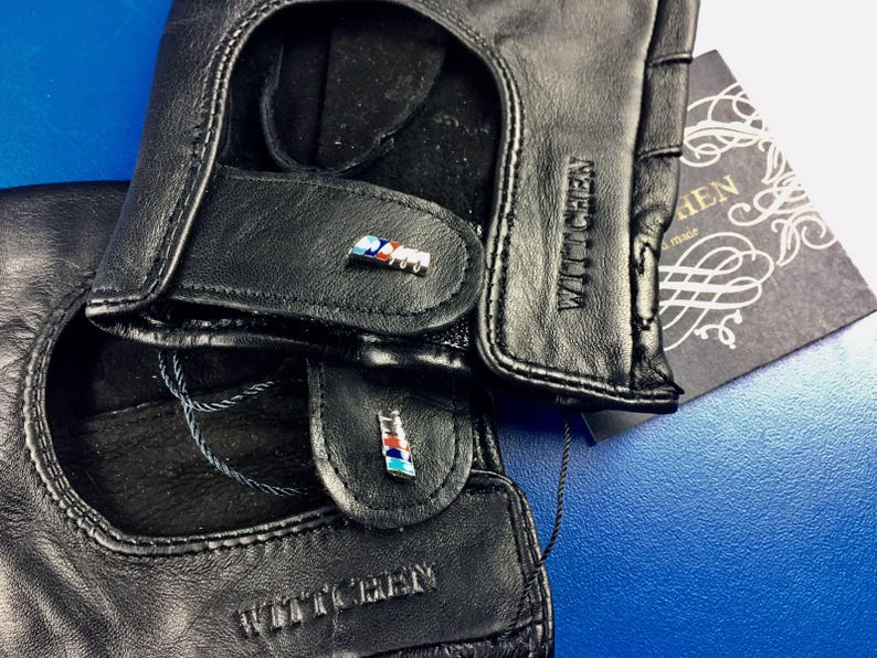 May include: A pair of black leather driving gloves with a blue, white, and red accent on each glove. The gloves have the text "WITTCHEN" embossed on the back of each glove.